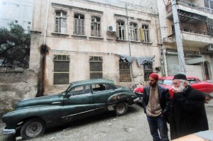 Mohamed Badr al-Din (R) stands in front of his vintage cars along a street where he keeps them, in the al-Shaar neighborhood of Aleppo